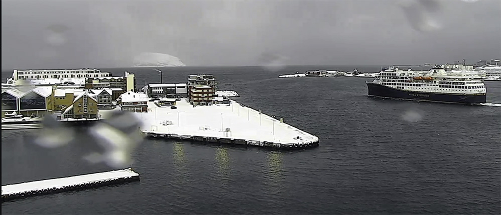 Sørgående kystrute Havila Capella gikk fra Hammerfest i sneelinger mandag ettermiddag den 19. februar 2024. Frisk bris fra vest. Pluss én grad. 
   Klikk på bildet og se mer. (Skjermklipp fra Bjost webkamera)